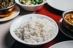 white rice is in a bowl on a table with other plates and bowls around it