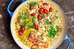 a pan filled with corn and tomatoes on top of a wooden table next to a spoon