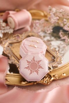 a close up of a mirror on a table with pink fabric and flowers in the background