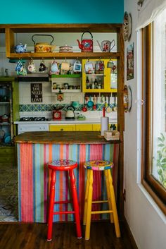 two brightly colored stools sit in front of a colorful kitchen counter with shelves on the wall