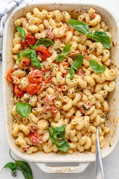 a casserole dish filled with pasta, tomatoes and basil