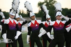 a group of women in black and red uniforms marching on a field with white feathers