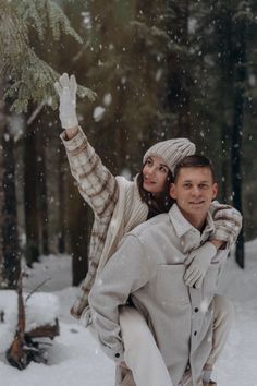 a man carrying a woman on his back in the snow while she is holding a small tree