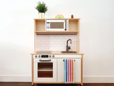 a toy kitchen with sink, stove and microwave in it's cupboards next to a potted plant