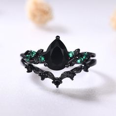 a black diamond ring with green stones on it's sides and leaves around the band