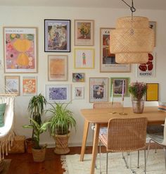 a dining room table with chairs and pictures on the wall above it, along with hanging plants