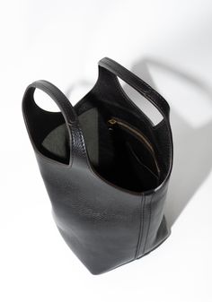 Ama Bag in Black from Lindquist. Small tote bag with hand carry bucket that widens gradually to form an undulating swooped top edge. Features circular handles and an interior drop pocket with zipper and card slot. Made from fully vegetable tanned milled leather is soft and supple, with a natural pebble from the tumbling process. Need a second opinion? If you have special requests or just need advice, please reach out to hello@shop-vestige.com. 100% Vegetable tanned and tumbled milled leather. Ma Black Bucket Shoulder Bag With Top Carry Handle, Bucket Shoulder Bag With Handle Drop For Errands, Bucket Bag With Top Carry Handle For Errands, Everyday Bucket Shoulder Bag With Rolled Handles, Travel Bucket Satchel With Rolled Handles, Travel Bucket Bag With Rolled Handles, Luxury Bucket Shoulder Bag With Rolled Handles, Bucket-style Satchel With Top Carry Handle For Travel, Black Hobo Bag With Rolled Handles