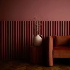 a vase sitting on top of a wooden table next to a brown couch in front of a red wall