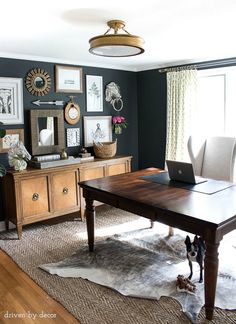 a desk with a laptop on top of it in front of a wall full of pictures