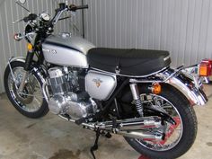 a silver motorcycle parked in front of a metal building with a black seat on it