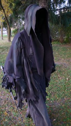 a person wearing a black hooded jacket and holding a stick in the grass with trees in the background