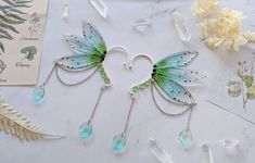 two fairy wings with chains attached to them on a table next to crystals and flowers