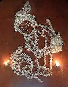 a sculpture made out of flowers and candles on a tile floor in front of a wall