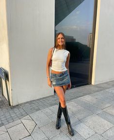 White high neck tank, jean medium wash mini skirt, black tall boots Denim Mini Skirt Outfit Spring, Summer Miniskirt Outfits, Jean Skirt Going Out Outfit, Denim Skirt Going Out Outfit, Jean Miniskirt Outfits, Chill Bar Outfit, La Outfits Summer, Spain Spring Outfits, Cool Going Out Outfits