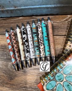 several pens are lined up on a wooden table next to a notebook and pen holder