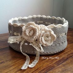 a crocheted basket with two flowers on the side and ribbon tied around it