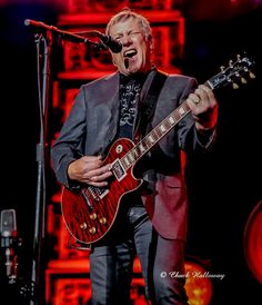 a man in a suit and tie playing an electric guitar on stage with a microphone