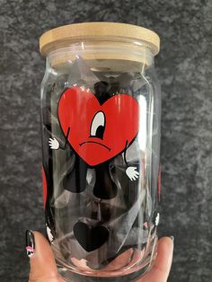 a hand holding a glass jar with a heart painted on the lid and an angry face drawn on it