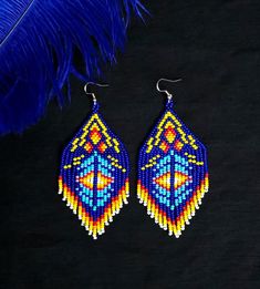 a pair of beaded earrings sitting on top of a black surface next to a blue feather