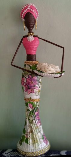 a doll holding a tray with flowers on it's head and wearing a pink top