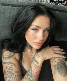 a woman with tattoos on her arms and chest sitting in a chair looking at the camera