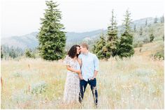 an engaged couple standing in the middle of a field with mountains in the back ground