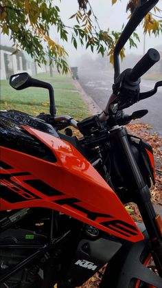 an orange and black motorcycle parked on the side of a road next to a tree