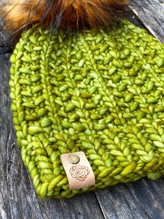 a green beanie with a brown pom - pom sits on an old wooden surface