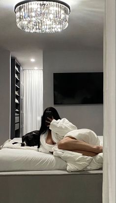 a woman laying on top of a bed under a chandelier next to a black cat