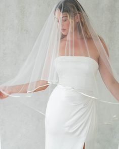 a woman in a white dress wearing a veil and holding her hand out to the side