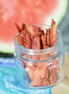 a glass jar filled with pieces of bacon next to a slice of watermelon