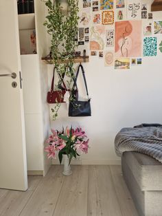 a bedroom with white walls and wooden floors has pictures on the wall, flowers in a vase next to a bed