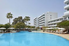 an empty swimming pool with lounge chairs and umbrellas in front of the hotel buildings