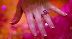 a close up of a person's hand with a ring on her finger and pink lights in the background