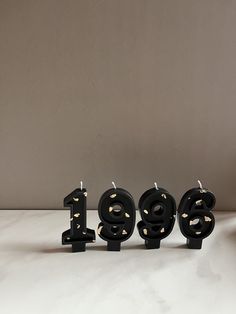 three black candles with gold numbers are sitting in front of a white wall and the word boo spelled out