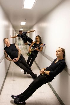 three men are standing in a hallway with guitars and one man is laying on the floor