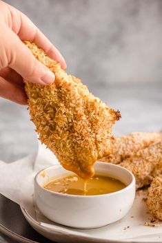 a person dipping chicken tenders into a bowl of sauce on top of a plate