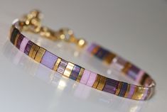 a close up of a bracelet on a white surface with gold and purple beads in it