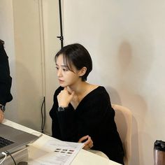 a woman sitting in front of a laptop computer on top of a white desk next to a cup