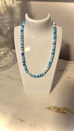 a necklace is sitting on a white display stand in front of a vase with flowers