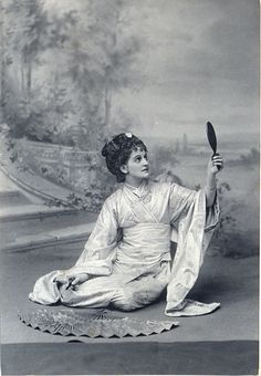 an old photo of a woman sitting on the ground with a mirror in her hand