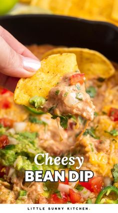 a hand holding a tortilla chip over a bowl of cheesey bean dip