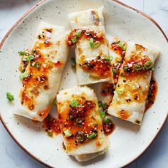 a white plate topped with dumplings covered in sauce and green onions on top of a marble table