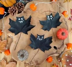 three black leaves on a wooden board surrounded by oranges and other autumn decorations including pine cones