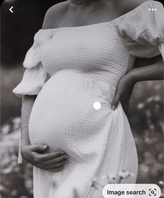 a pregnant woman in a white dress with her hand on her belly, looking at the camera