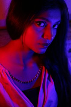 a woman with long black hair and blue eyes is looking at the camera while wearing a necklace