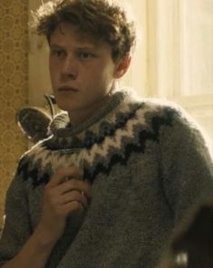 a young man holding a spoon in his right hand and looking at the camera while wearing a sweater