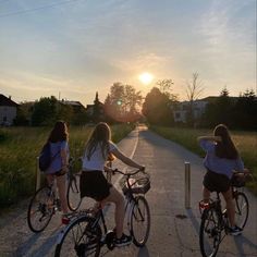 three girls riding bikes down a road at sunset