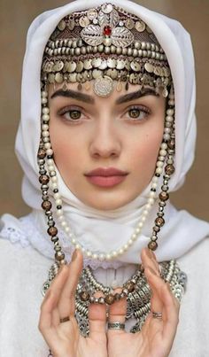 a woman wearing a headdress with pearls and jewelry on her face, holding hands together