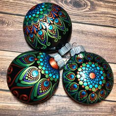 three colorful ornaments are sitting on a wooden surface, one is painted black and the other is multicolored